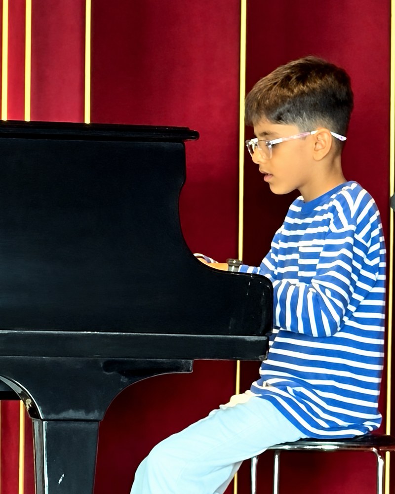 Aveer playing a grand piano on stage in front of a red curtain